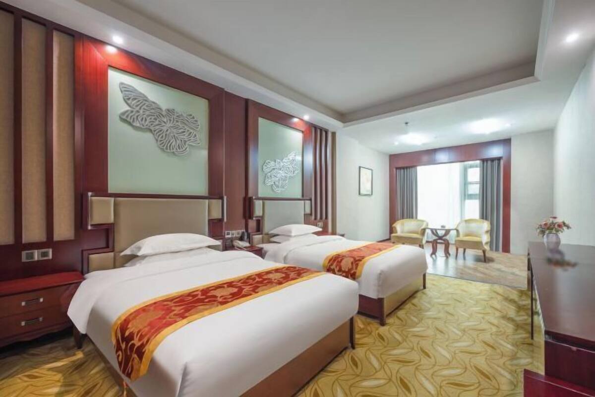 Une chambre d’hôtel avec deux lits, un bureau, une chaise et un élément décoratif mural.