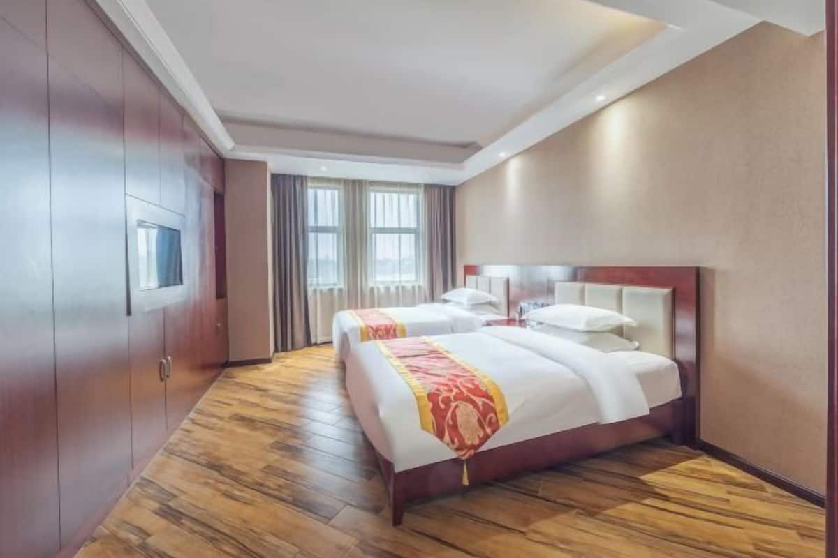 Une chambre d’hôtel avec deux lits, une télévision, une fenêtre avec des rideaux et un plancher en bois.