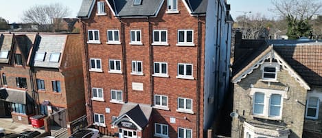 A multi-story residential building with a brick facade, multiple windows, and a parking area with cars.
