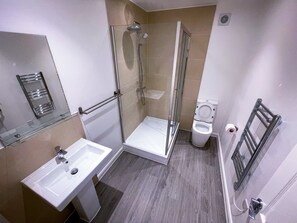 A modern bathroom with a glass shower enclosure, a white sink, and a toilet. - Ilford Apartments (Ilford)