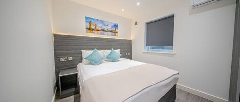 A modern bedroom with a bed, bedside tables, a nightstand, a window, and an air conditioning unit.