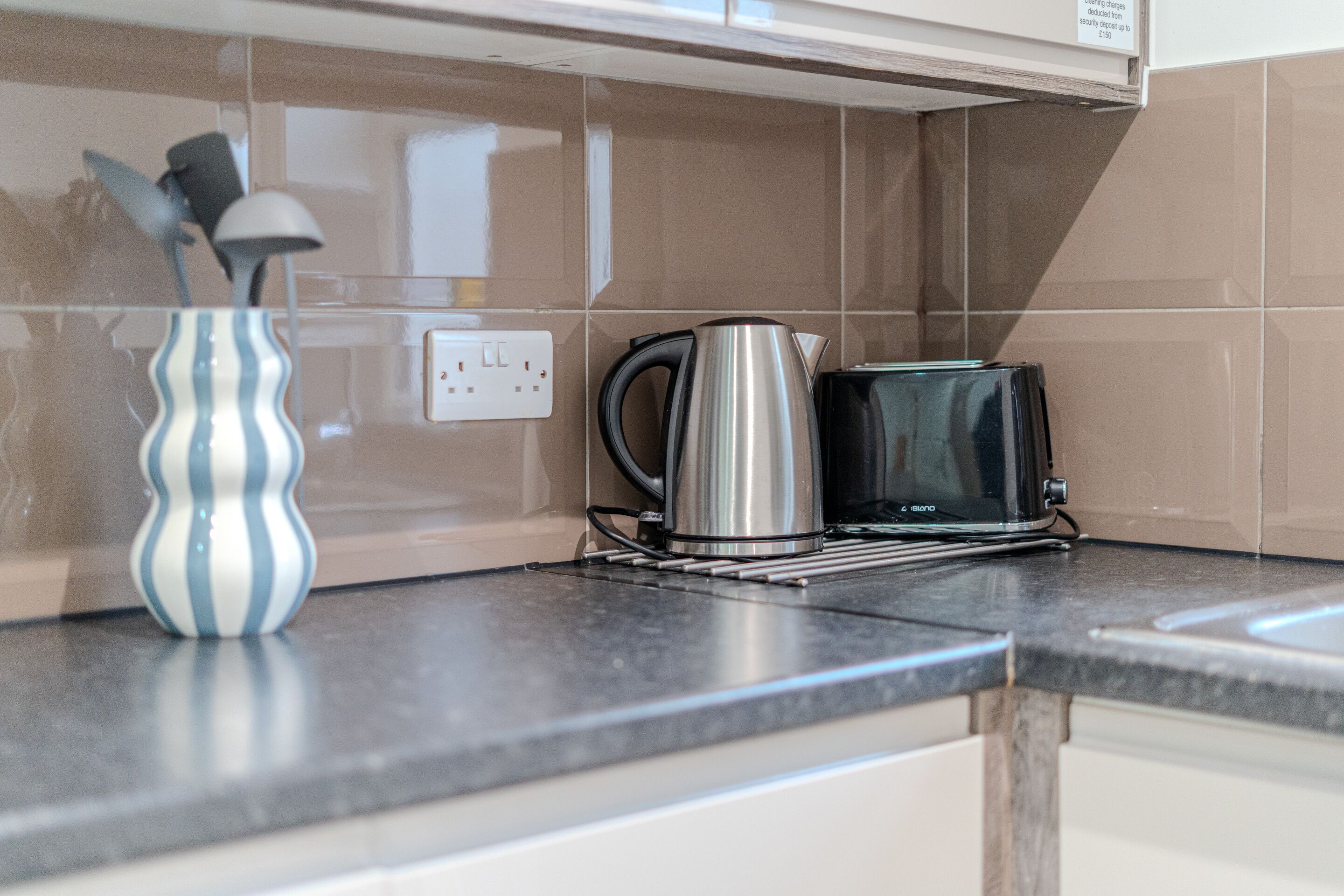 A kitchen counter with a kettle, toaster, and a striped vase.