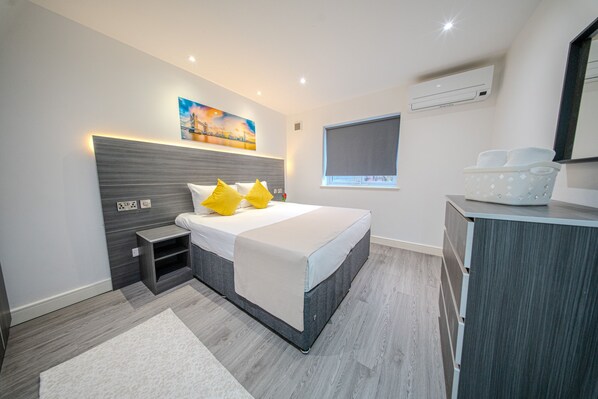 A modern bedroom with a bed, bedside tables, a nightstand, a dresser, and a painting on the wall. - Ilford Apartments (Ilford)
