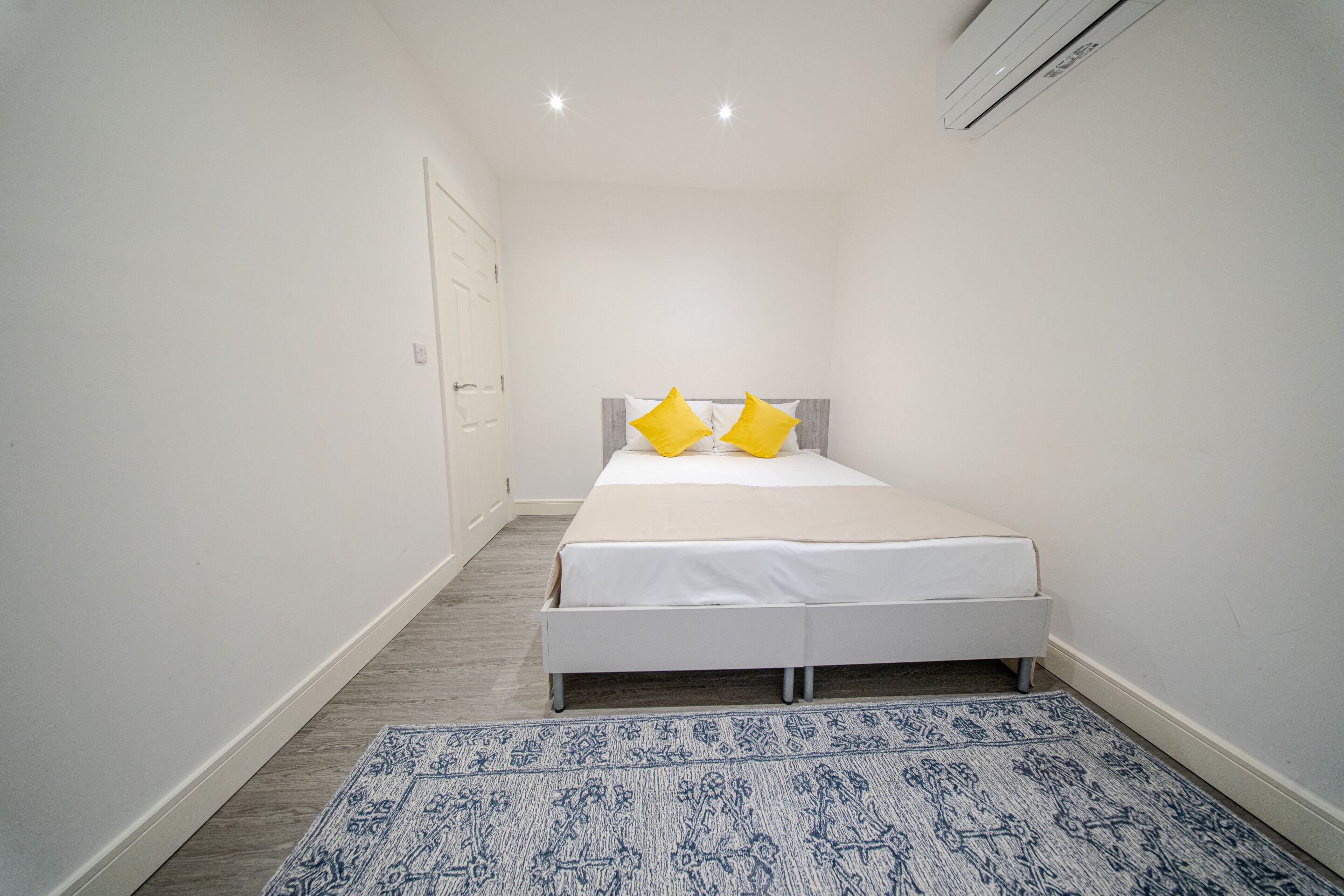 A bedroom with a bed, two pillows, a patterned rug, and a white wall.