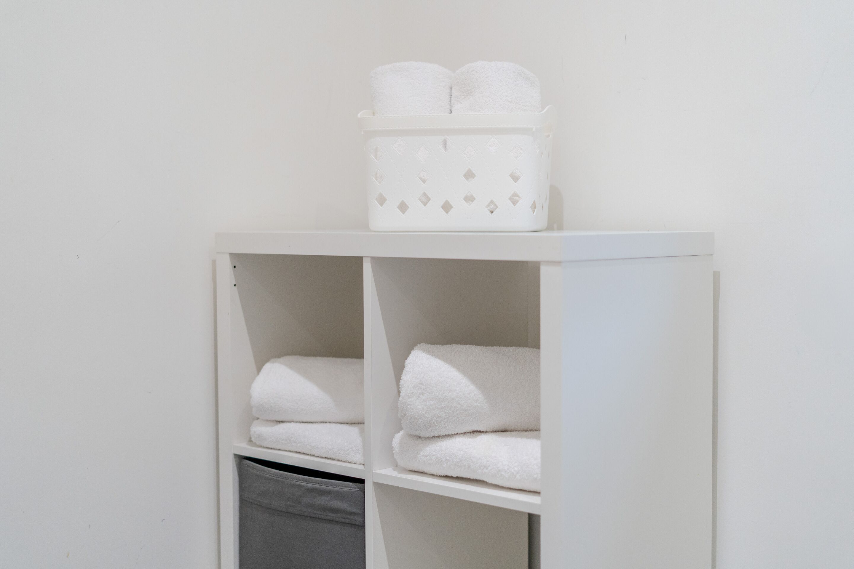 Een witte kast met planken waarop opgevouwen handdoeken liggen en een mand met opgerolde handdoeken.