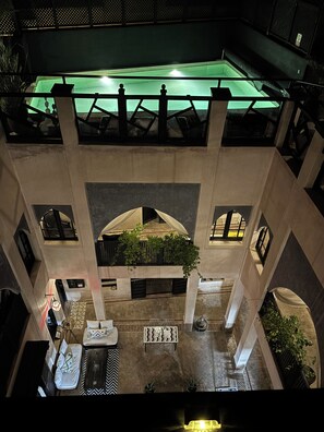Un edificio a più livelli con un cortile centrale, balconi e una piscina illuminata di verde.
