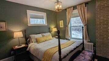 Quarto com cama de dossel, mesa de cabeceira com luminária, janela com cortinas e radiador.