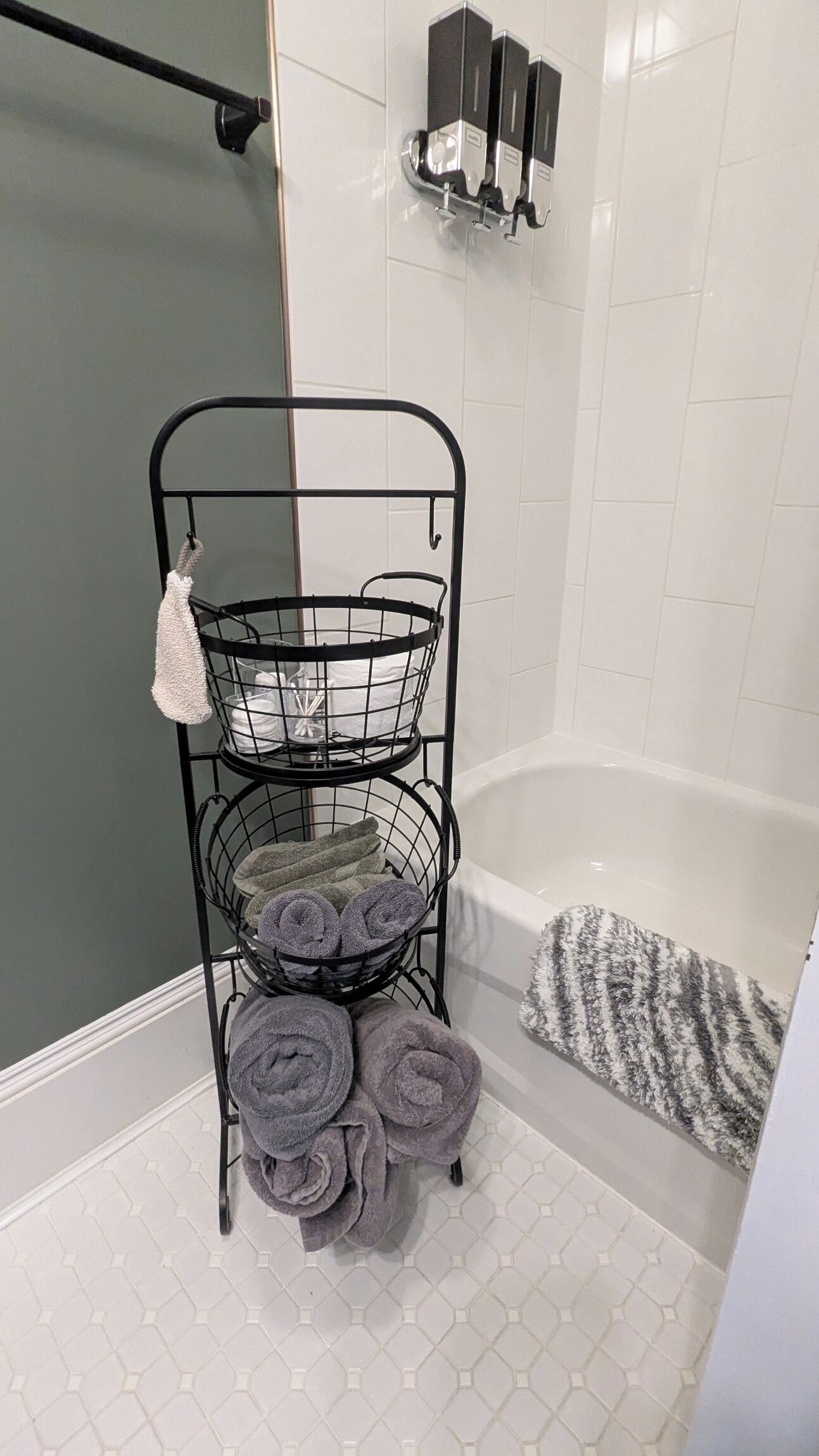 A bathroom with a metal towel rack holding folded towels, a shower area, and a white tiled wall.