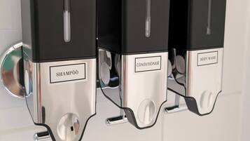 A wall-mounted dispenser with three compartments labeled 'SHAMPOO,' 'CONDITIONSER,' and 'BODY WASH.'