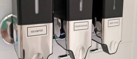 Dispensador de pared con tres compartimentos etiquetados 'SHAMPOO', 'CONDITIONSER' y 'BODY WASH'.