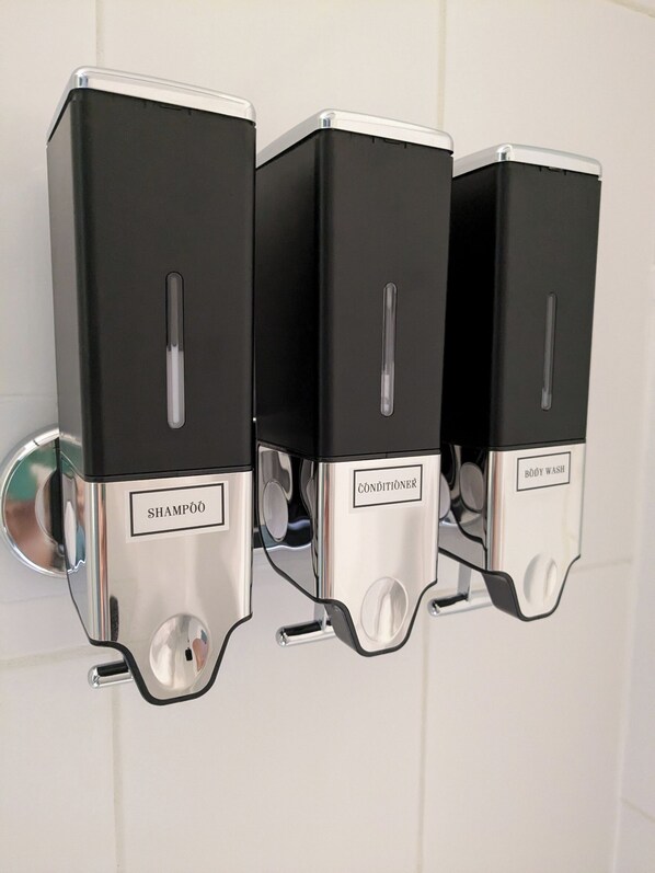 Dispensador de pared con tres compartimentos etiquetados 'SHAMPOO', 'CONDITIONSER' y 'BODY WASH'.