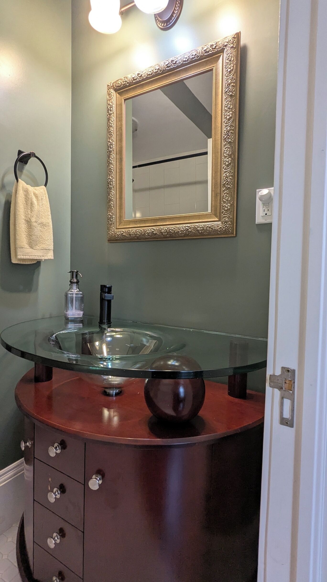 Une salle de bain avec un lavabo rond en verre, un meuble-lavabo en bois, un miroir avec un cadre doré et une serviette suspendue à un crochet.