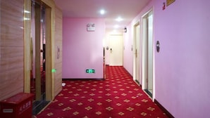 Um corredor de hotel com carpete vermelho, portas de madeira e parede rosa.