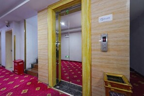 Et hotelværelse med rødt tæppe, trævæg, dør til glas elevator og et lille træbord.
