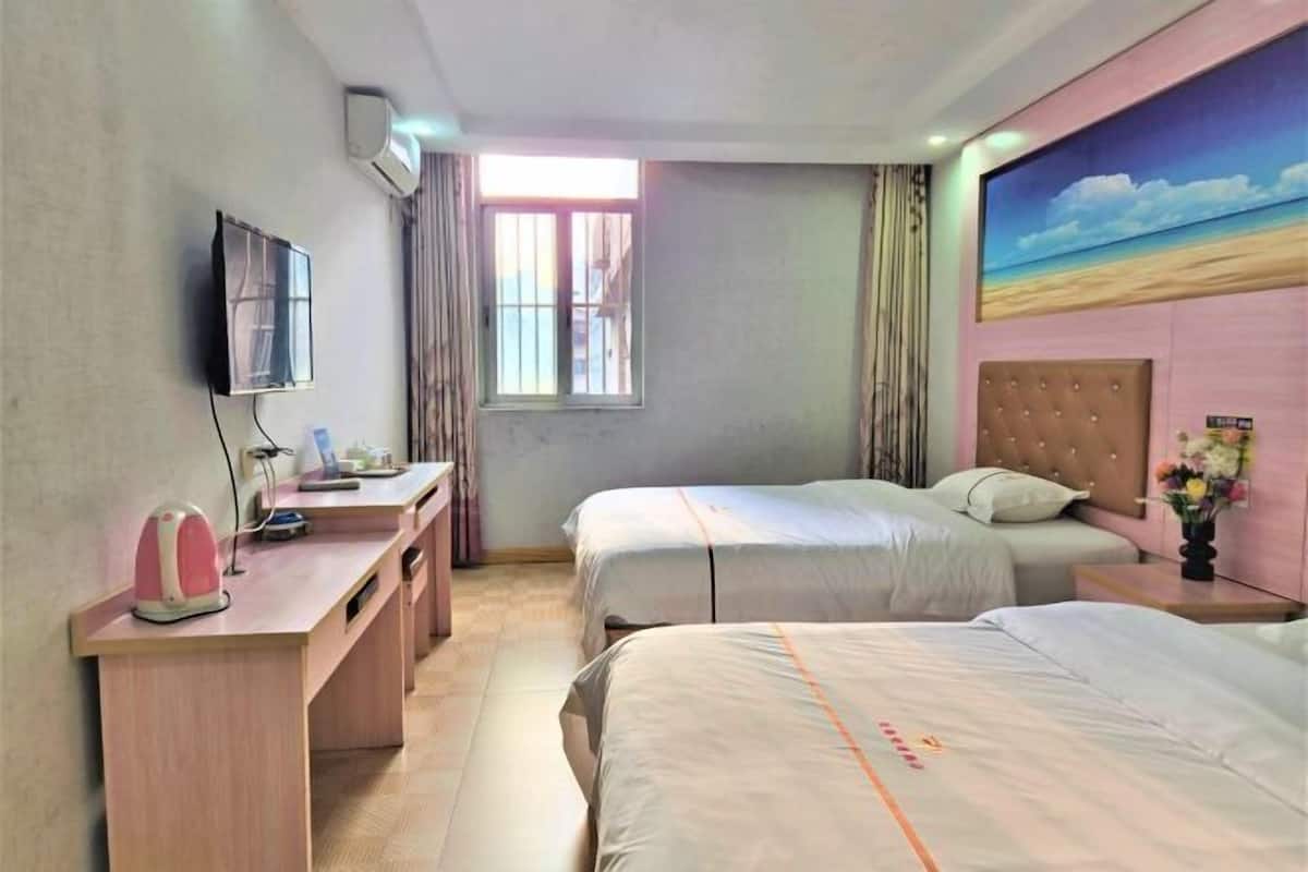 Quarto de hotel com duas camas, uma escrivaninha com chaleira, televisão e janela com cortinas.