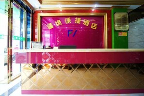 A reception desk with a red and pink color scheme, a glass partition, and a telephone. - Nanning Fengyuan Convenient Hotel No. 1 Affiliated Hospital of Medical University (Nanning)