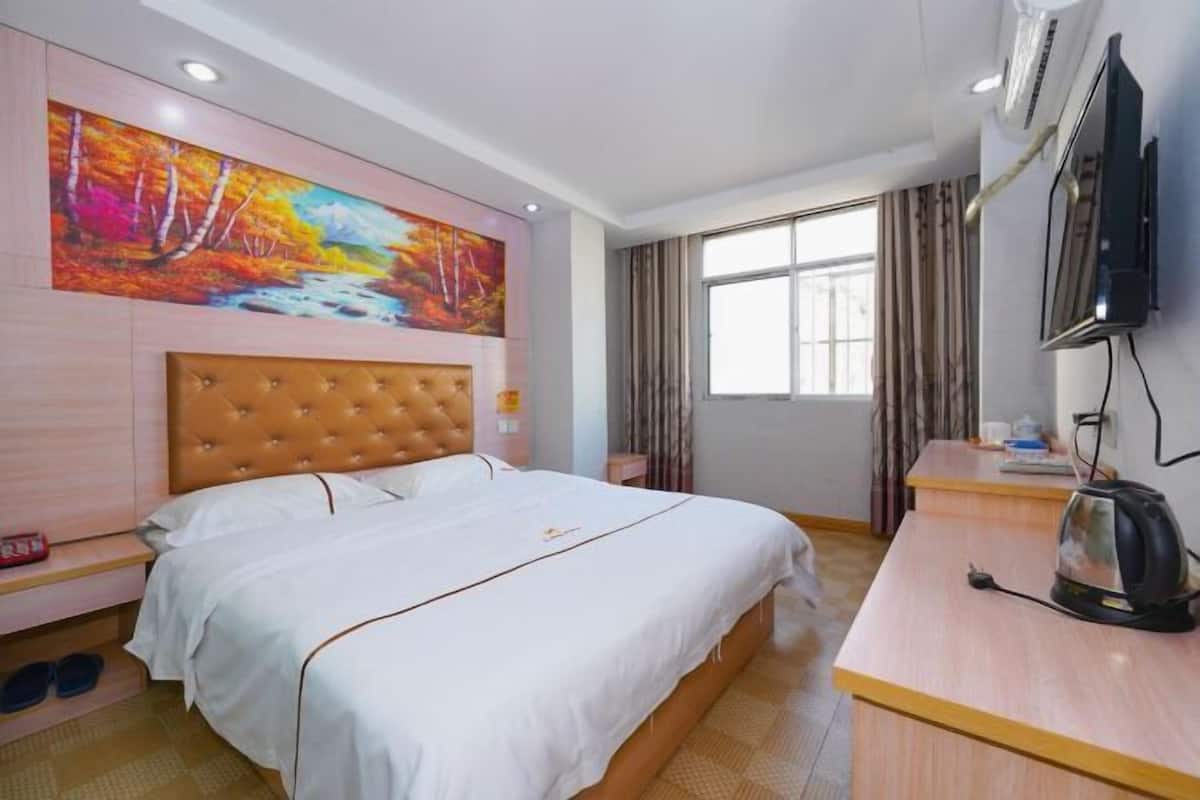 Quarto de hotel com uma cama grande, televisão, escrivaninha com chaleira e um quadro na parede.