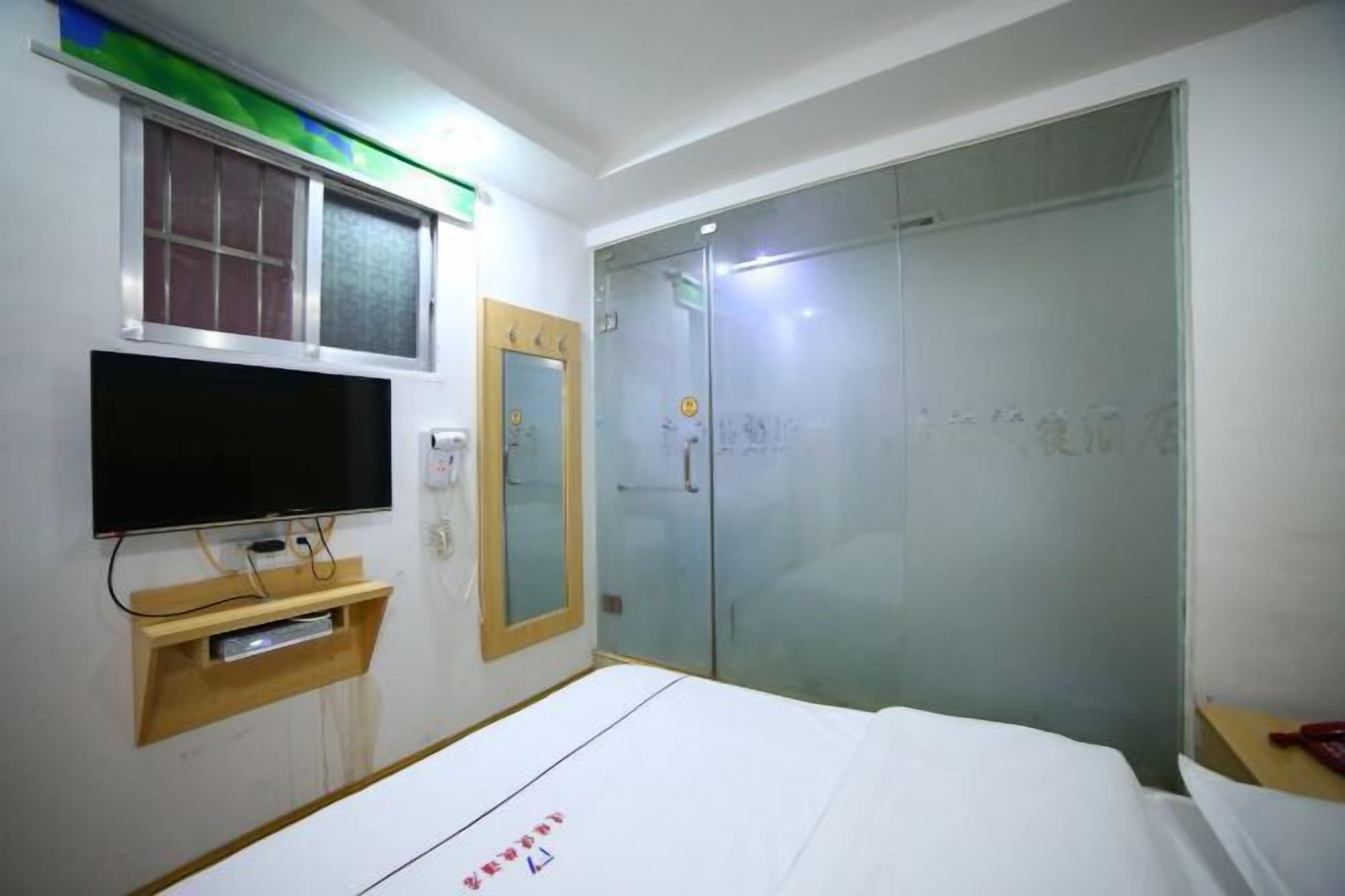 Una habitación de hotel con cama, televisión montada en la pared, armario y puerta corredera de cristal.