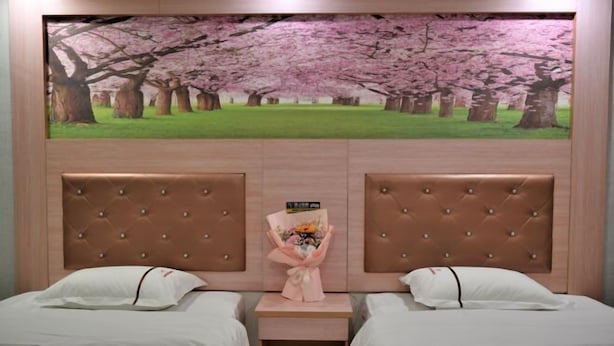 Quarto de hotel com duas camas, uma pintura grande de cerejeiras e um buquê de flores na mesa de cabeceira.