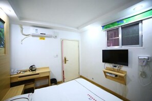 A hotel room with a bed, a desk, a TV, an air conditioning unit, and a window with blinds. - Nanning Fengyuan Convenient Hotel No. 1 Affiliated Hospital of Medical University (Nanning)