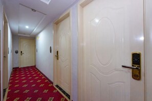 Un couloir d’hôtel avec un tapis à motifs, des portes blanches et une serrure numérique sur l’une des portes.