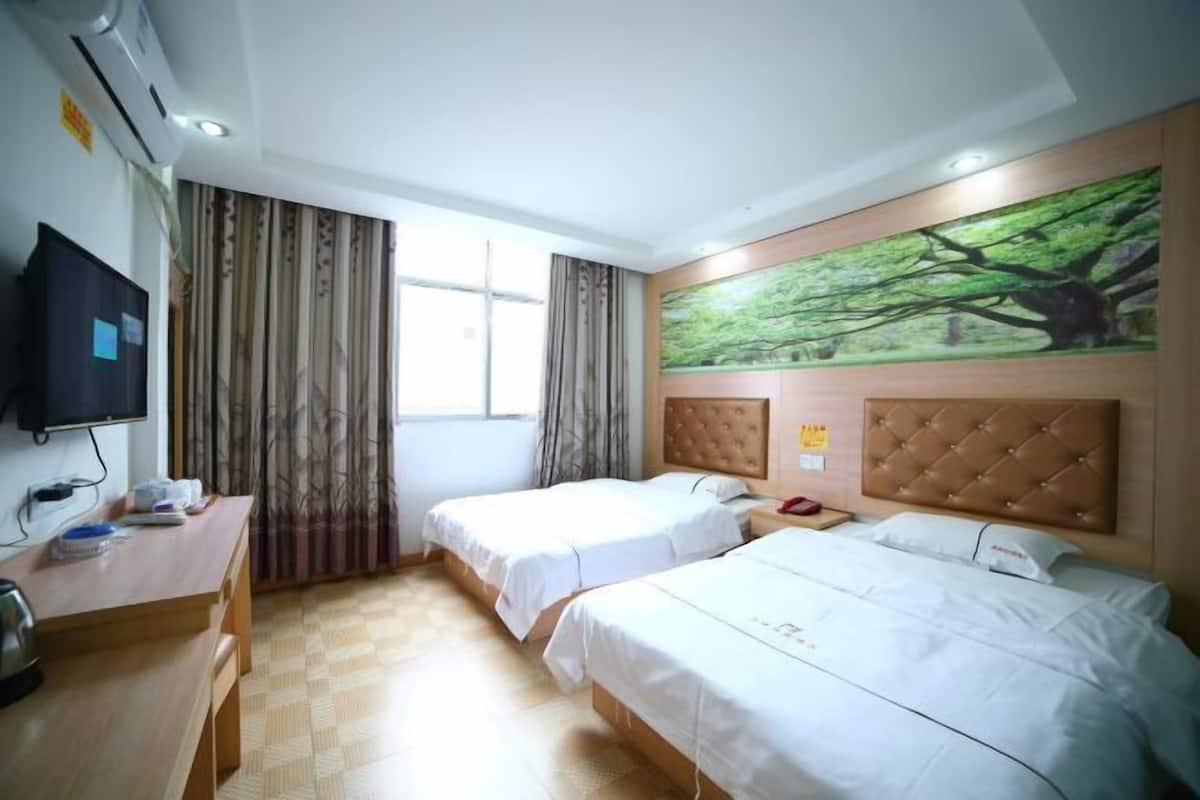 Quarto de hotel com duas camas de solteiro, uma escrivaninha com televisão e uma janela grande com cortinas.