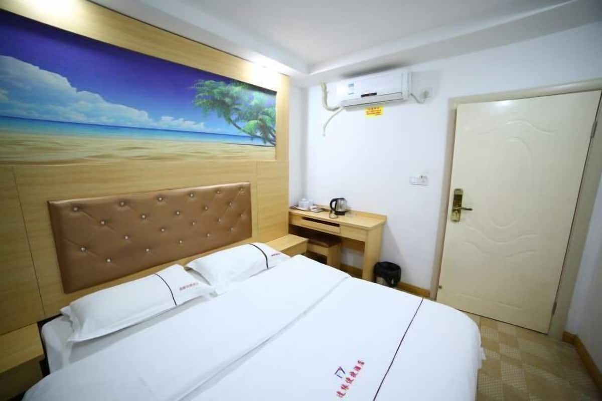 Quarto de hotel com uma cama, uma mesa, um quadro de uma praia e uma porta.