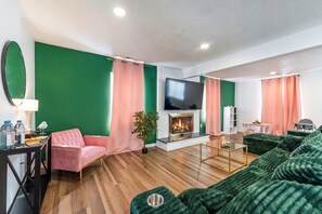 Uma sala de estar moderna com lareira, cortinas verdes e rosa, um sofá rosa e um sofá verde.