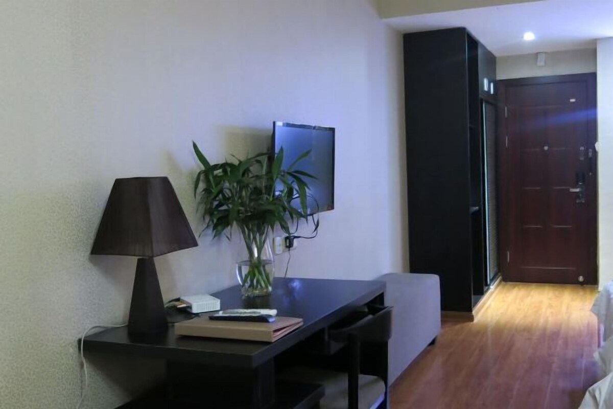 A room with a desk, a lamp, a plant, a television, and a door.