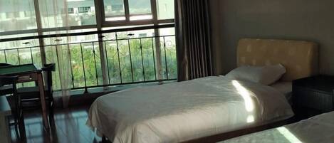Habitación de hotel con dos camas, una mesita pequeña y vistas a zonas verdes a través de amplios ventanales.