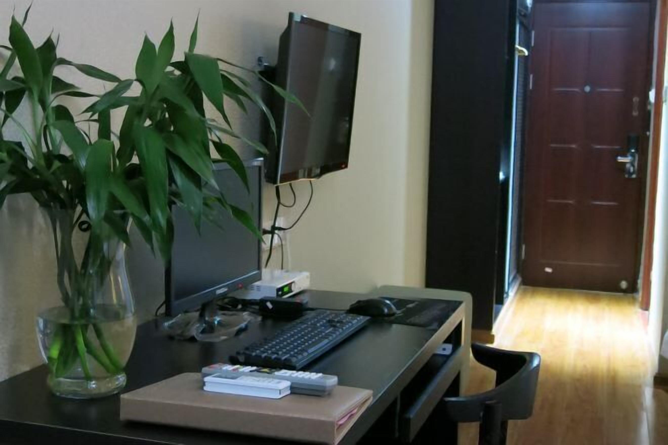 Una habitación con un escritorio, una computadora, teclado, ratón, monitor, una planta y una puerta.