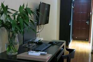 A room with a desk, a computer, a keyboard, a mouse, a monitor, a plant, and a door.