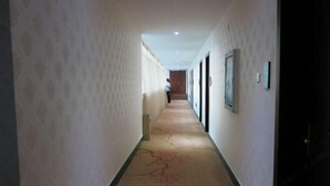 Een hotelgang met behang met een patroon, een vloerkleed met bloemenmotieven en ingelijste foto's aan de wanden.