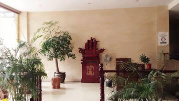 Un hall con mostrador de recepción, una pieza decorativa roja y plantas en macetas.