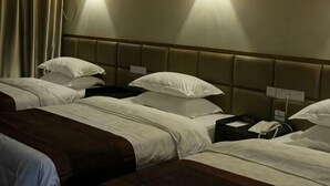 Een hotelkamer met drie bedden, een hoofdeinde, nachtkastjes en wandlampen.