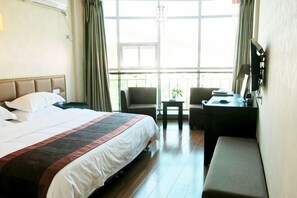 A hotel room with a large bed, a desk, a chair, and a small table. - Juntai Hotel (Taining)