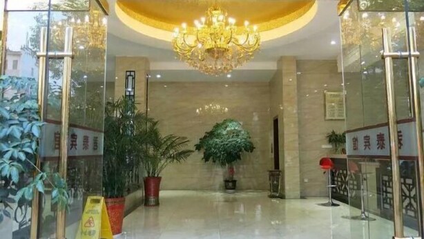 Een hotel lobby met een kroonluchter, potplanten en een rood tapijt.