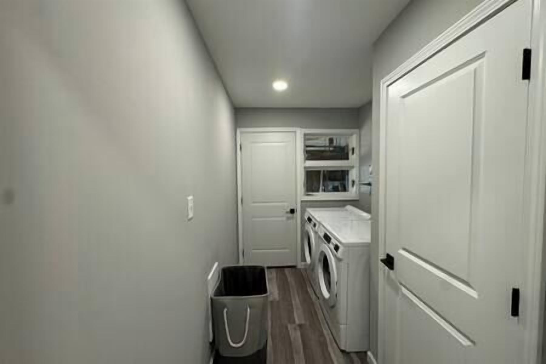 A laundry room with a washing machine, a dryer, and a small trash bin.