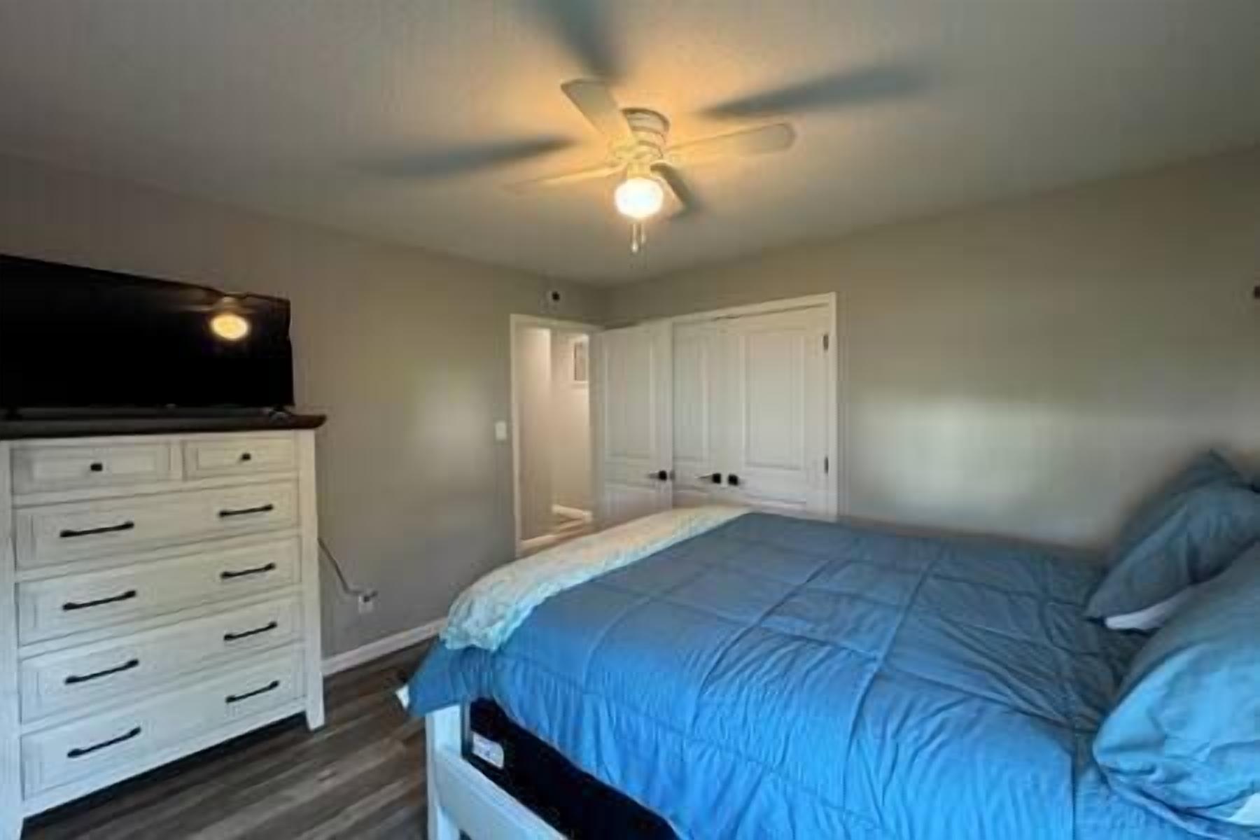 A bedroom with a bed, a dresser, a ceiling fan, and a door.