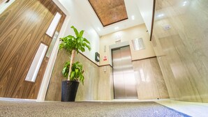 A modern lobby with a wooden door, a potted plant, an elevator, and a sign indicating a CCTV system. - Ilford Tower Apartments (Ilford)