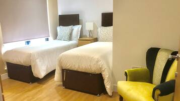 A hotel room with two beds, a nightstand, a chair, and a window.