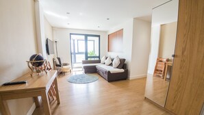 A modern living room with a wooden floor, a sofa, a coffee table, and a TV. - Ilford Tower Apartments (Ilford)