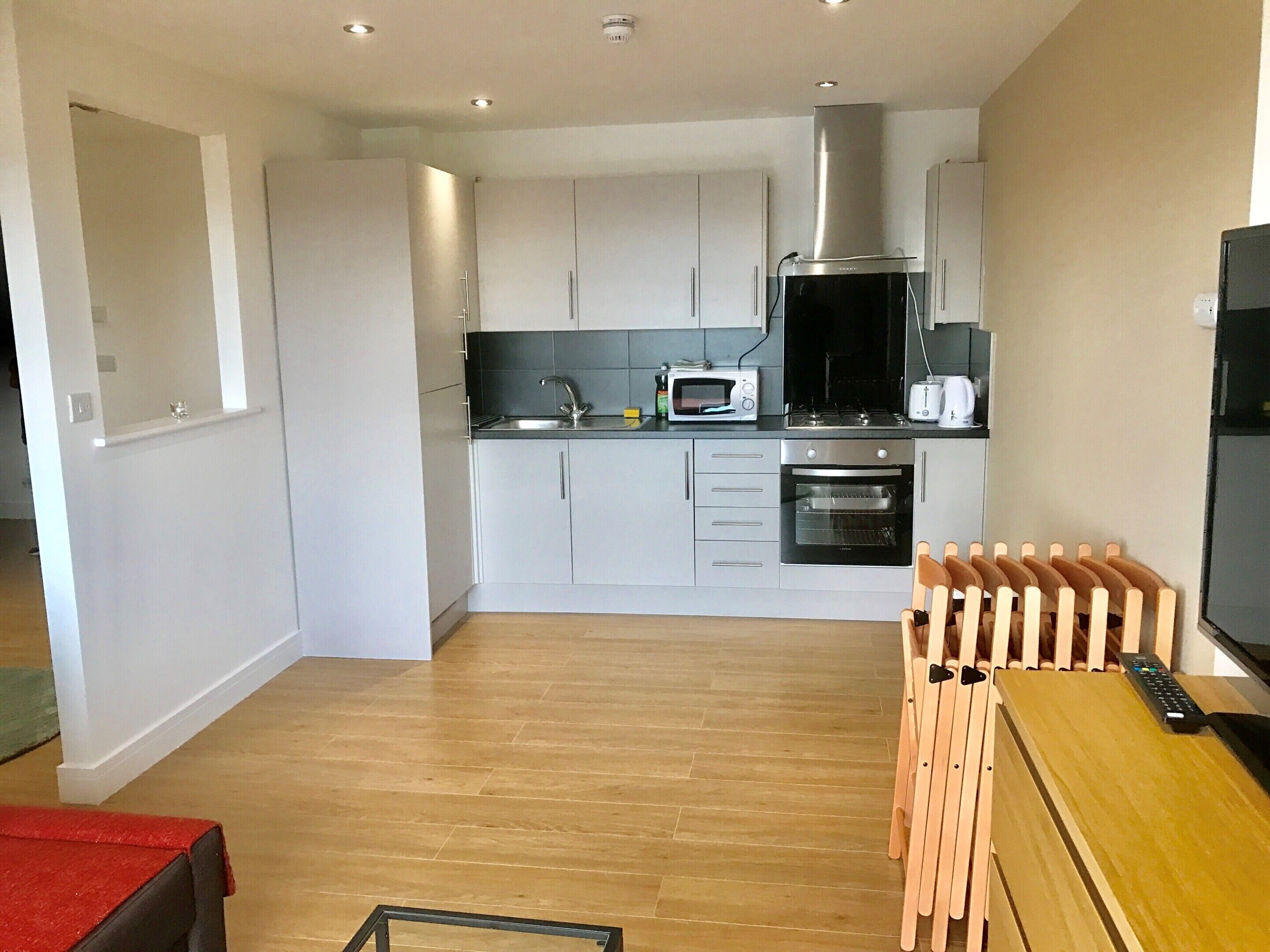 A modern kitchen with grey cabinets, a microwave, a stove, and an oven. There is a wooden table with chairs and a TV on the right side.