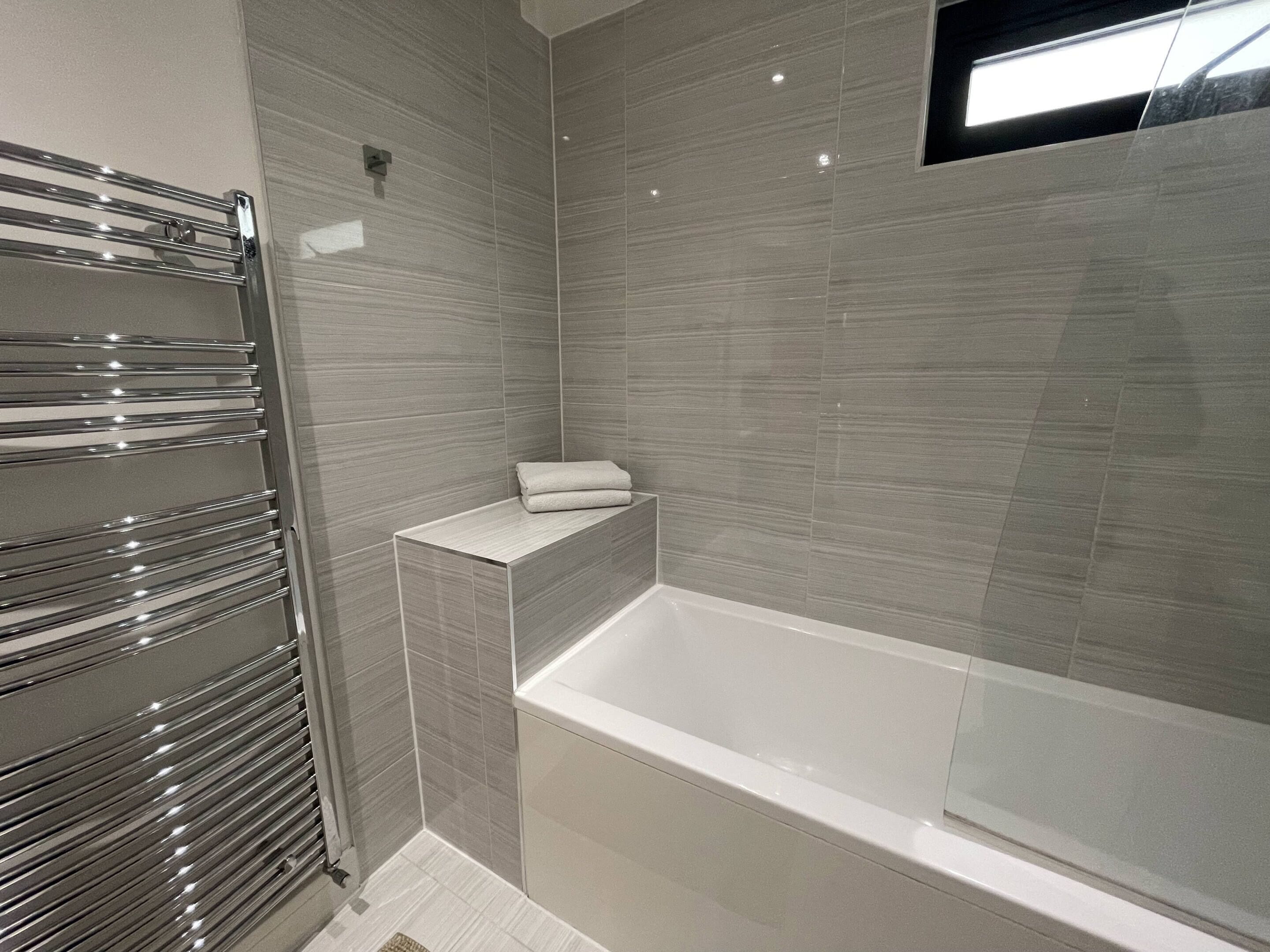A modern bathroom with a built-in bathtub, a towel rack, and a small shelf.