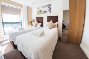 A hotel room with two beds, a large window, a painting, and a mirror. - Ilford Tower Apartments (Ilford)
