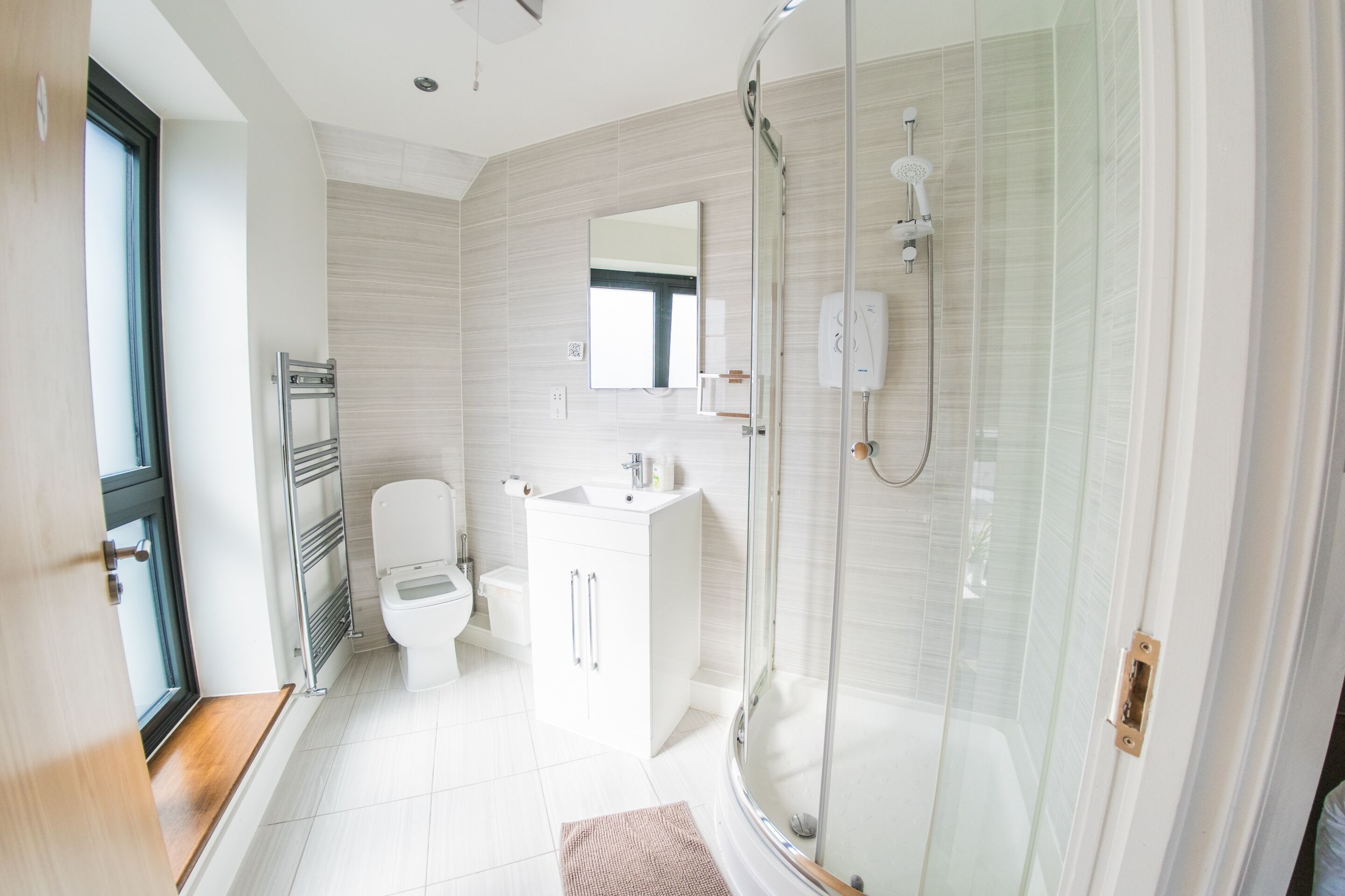 Et moderne badeværelse med et glasafskærmet brusebad, en hvid vask og et toilet.