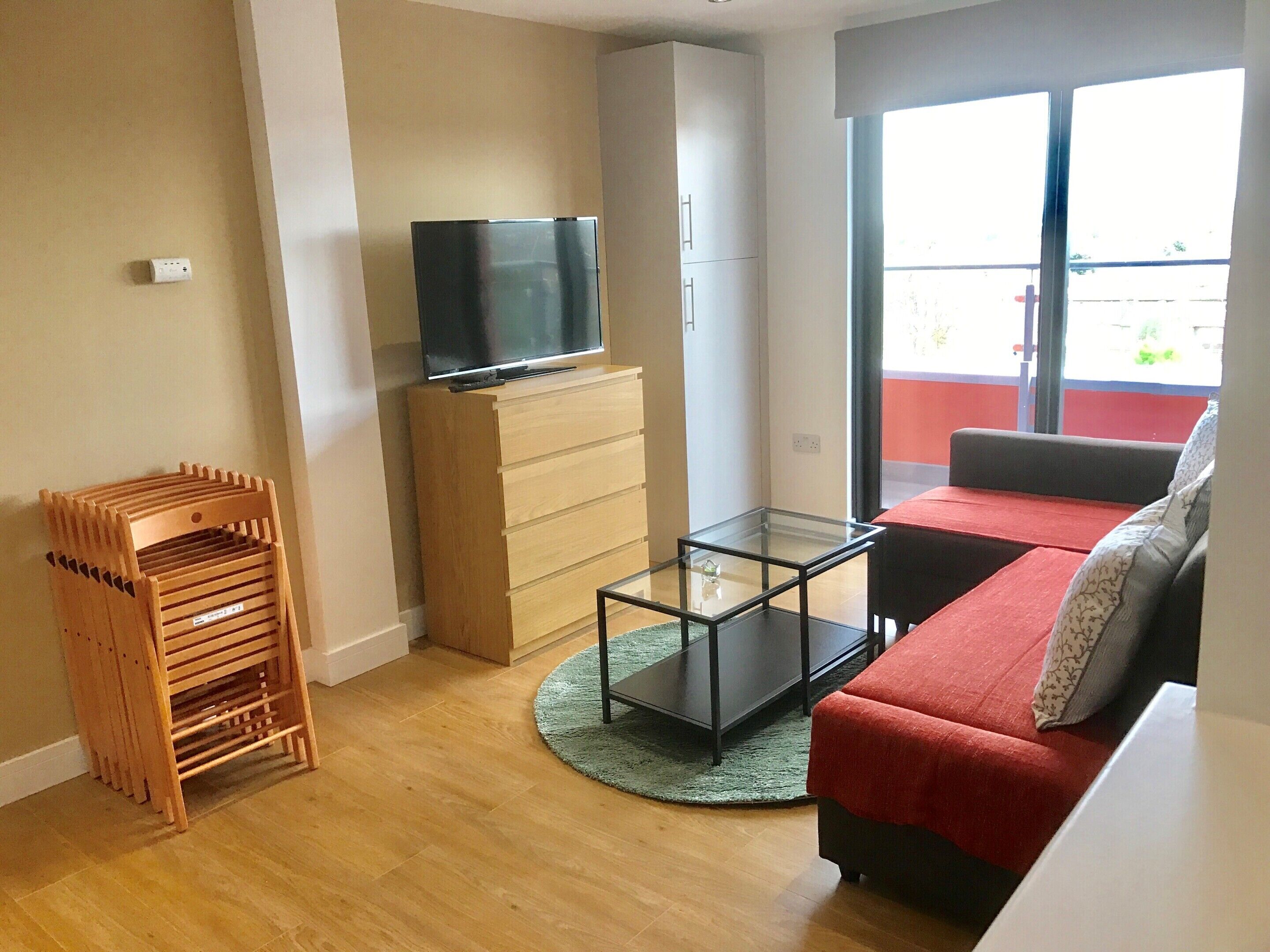 A modern living room with a sofa, a glass coffee table, a wooden TV stand, and a window with a view.