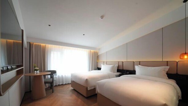 A hotel room with two beds, a desk, a chair, a TV, and a large window with curtains. - Zhongtai Hotel (Huangshan City)