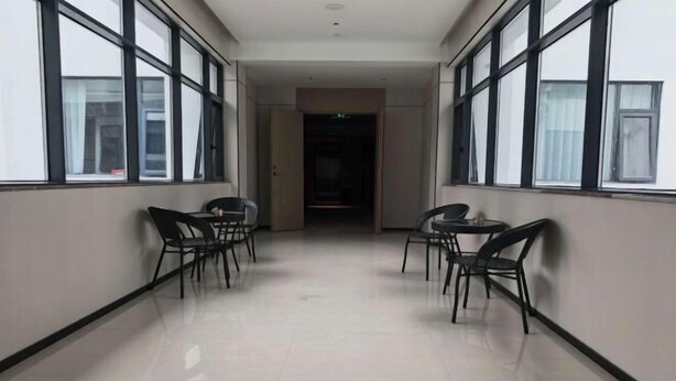 Un couloir avec des chaises et des tables, de grandes fenêtres et une porte au fond.