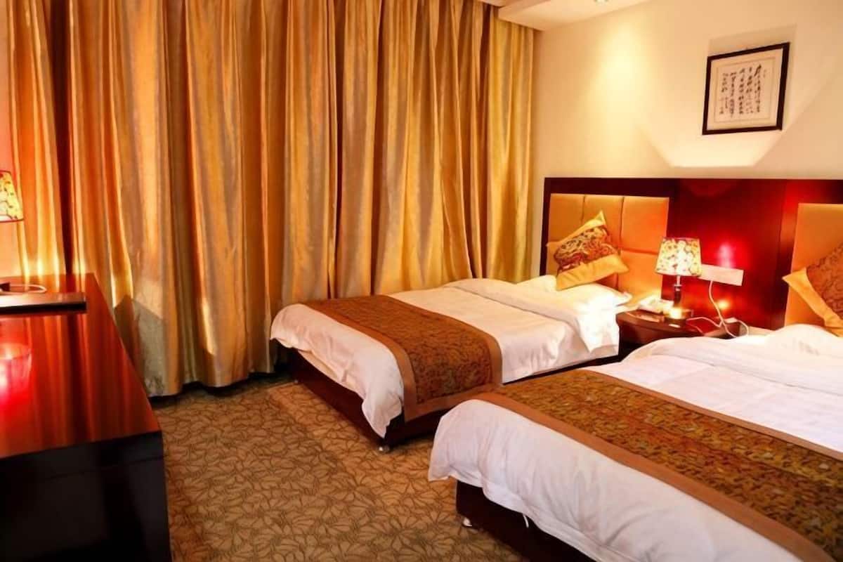 A hotel room with two beds, a desk, and a nightstand with lamps.